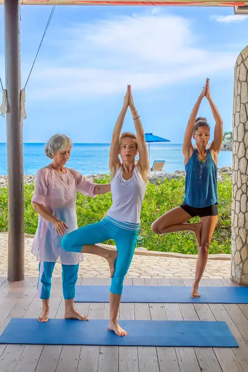 Group of people practicing a yoga pose on a wooden deck overlooking the ocean at Rockhouse Hotel in Negril, Jamaica, highlighting a serene wellness experience at Rockhouse Hotel.