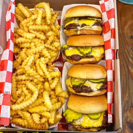 Heaping basket of golden crinkle-cut fries paired with two cheeseburgers from The Meat Up Grill, perfect for sharing.