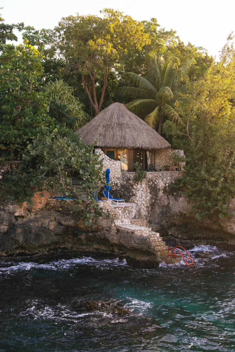 wooden footbridge leading to a cliffside cottage, overlooking the clear blue sea in Negril, Jamaica, highlighting the rustic charm and natural beauty of the area.