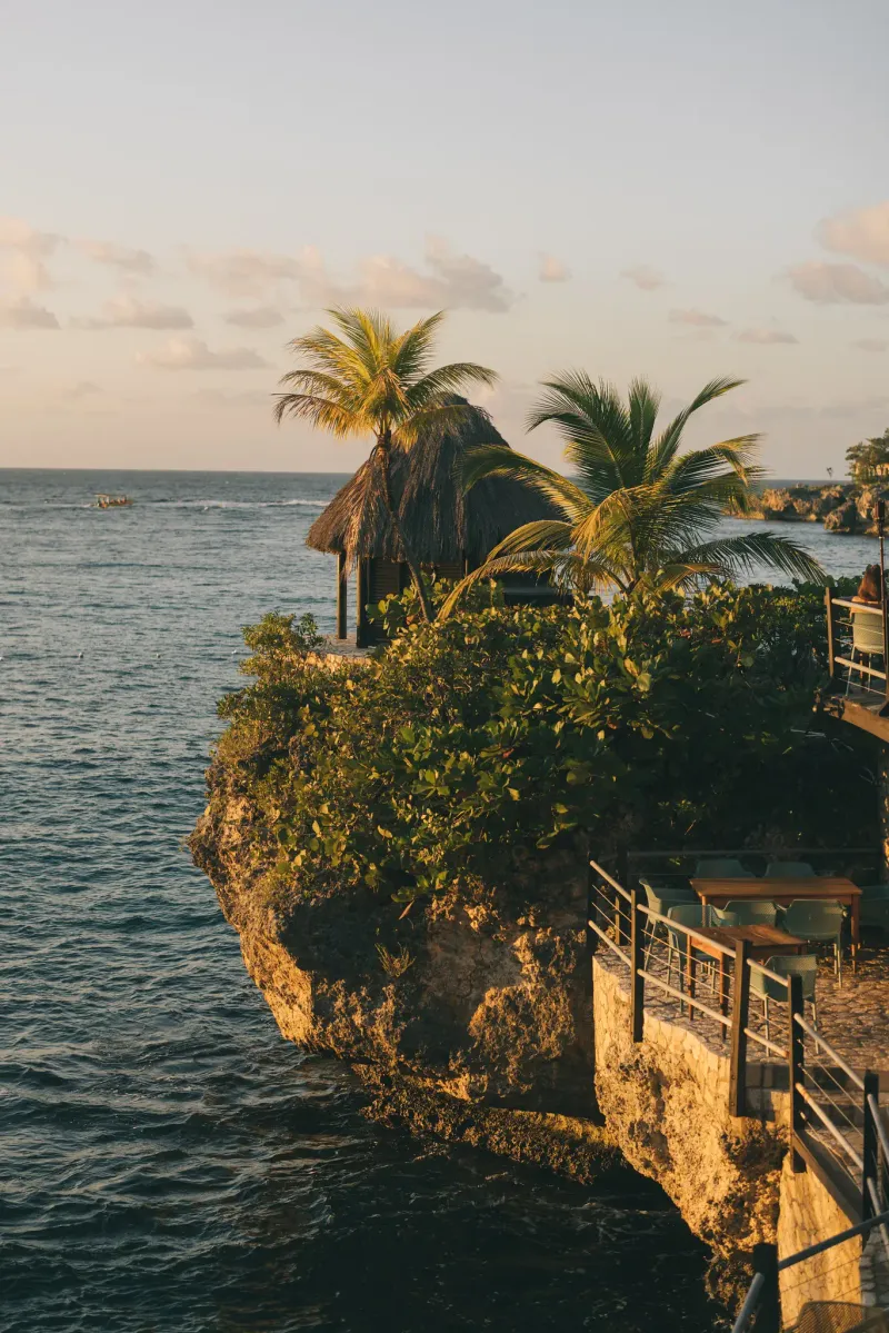 A high-angle view of Idle Awhile Cliffs'  terraced cliffs with palm trees and a small private deck, overlooking the calm Caribbean Sea in Negril, Jamaica, highlighting the intimate and secluded nature of the property.