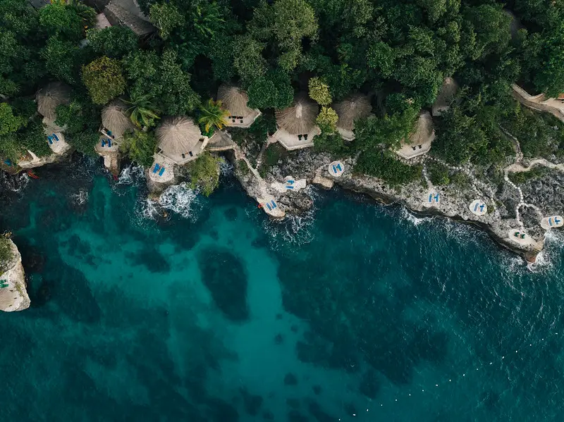 Aerial view of Rockhouse Hotel in Negril, Jamaica, showcasing thatched-roof villas nestled among lush greenery along the stunning turquoise Caribbean coastline.