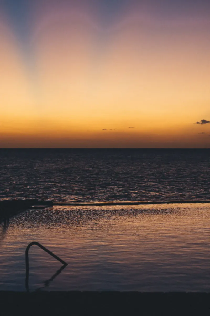 A serene sunset over the ocean at Rockhouse Hotel in Negril, Jamaica, with the golden light reflecting on the water and silhouetting the distant horizon, highlighting the resort's picturesque evening views.