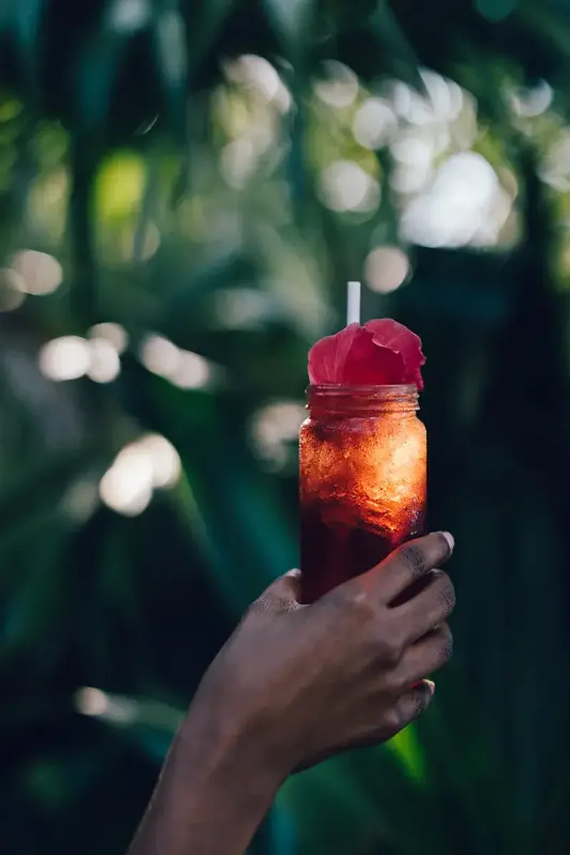 Cold cocktail in the hand of a guest with the backdrop of the lush tropical gardens at the Rockhouse Restaurant at Rockhouse Hotel in Negril, Jamaica.