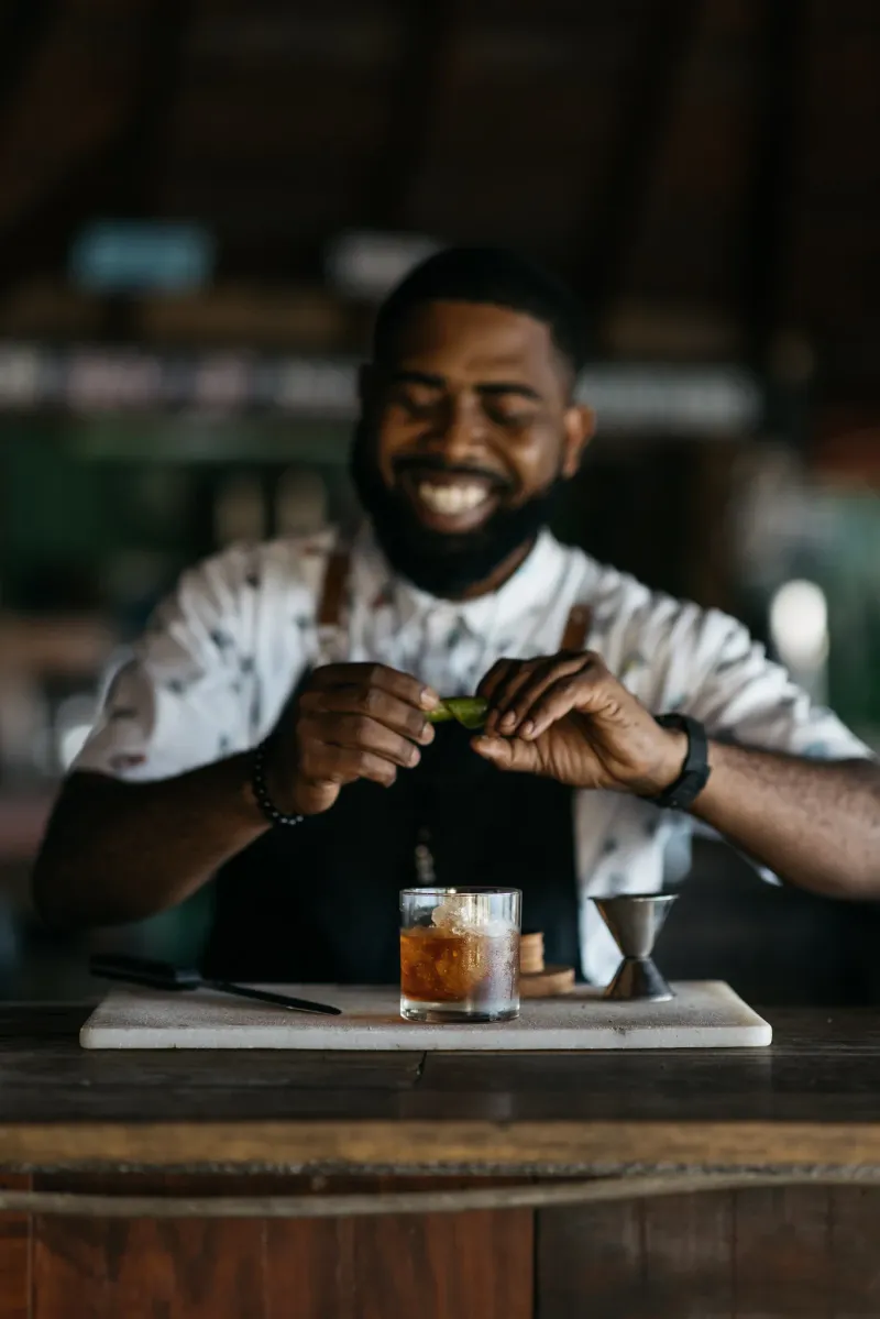 The smiling face of the award winning bartender making an old fashioned cocktail at the bar at Rockhouse Restaurant at Rockhouse Hotel in Negril, Jamaica.