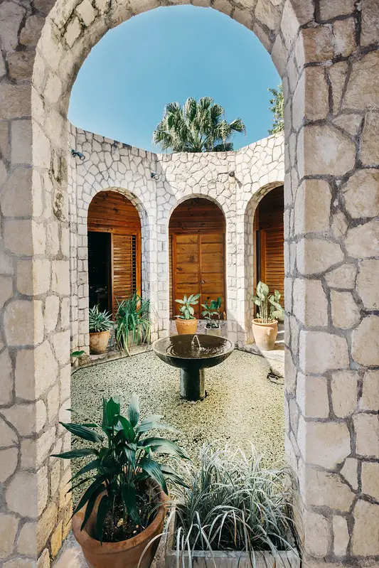 Stone courtyard at Rockhouse Hotel in Negril, Jamaica, featuring a central fountain, potted tropical plants, and arched doorways, offering a serene and elegant retreat