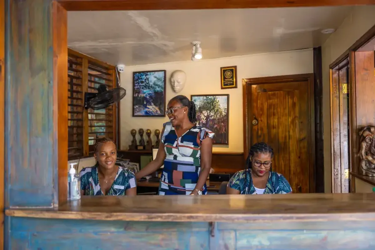 Three women at the front desk of Rockhouse Hotel in Negril, Jamaica, smiling and ready to assist guests—a warm welcome from the hotel staff.