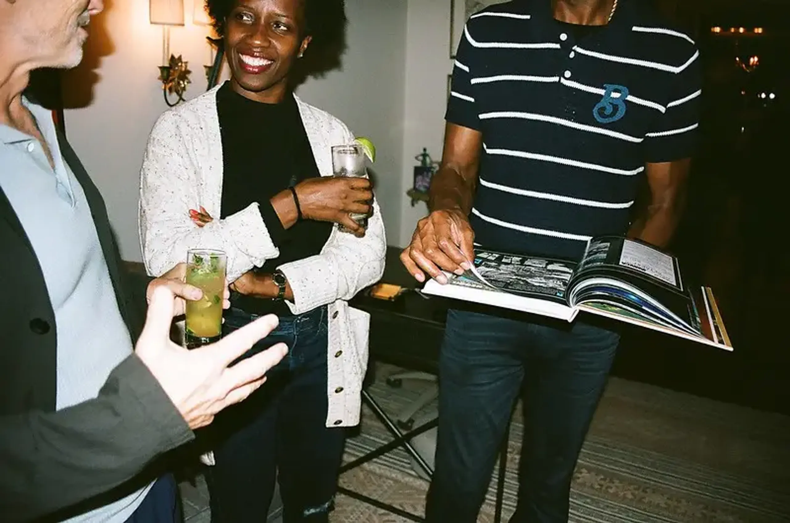 People enjoying drinks and conversation while looking at a book during a social event at Rockhouse Hotel in Negril, Jamaica, highlighting a lively gathering at Rockhouse Hotel.