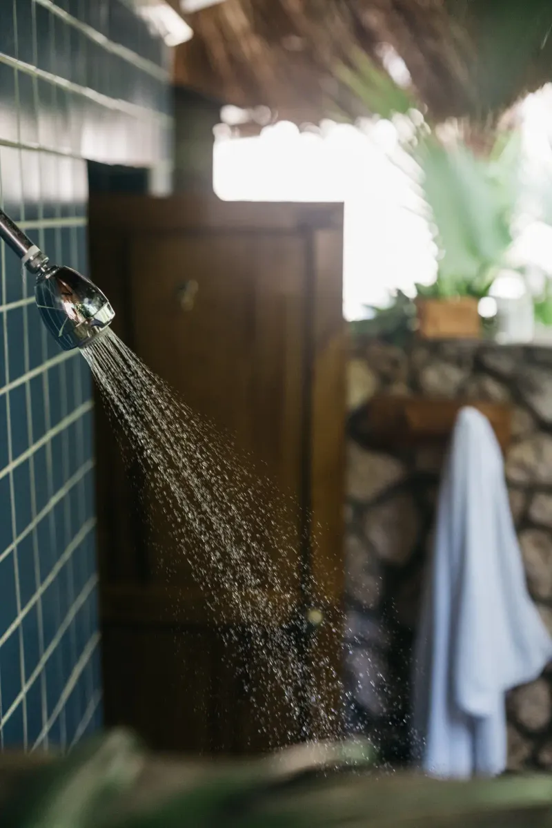 A scenic view of a curved stone balcony with a closed blue umbrella and a lounge chair at Rockhouse Hotel in Negril, Jamaica, overlooking a beautiful sunset over the sea, highlighting the resort's picturesque evening setting.