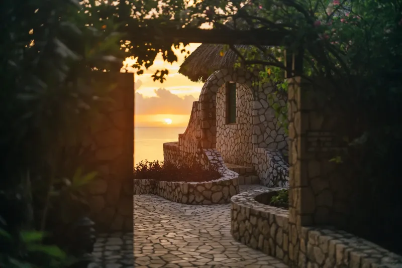 A winding stone path at Rockhouse Hotel in Negril, Jamaica, with a beautifully lit archway at night, showcasing the resort's charming architecture and secluded walkways.