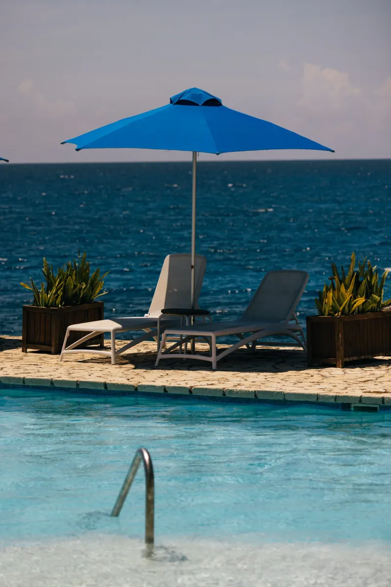 Two lounge chairs and under an open umbrella by the pool, overlooking the Caribbean Sea at Rockhouse Hotel in Negril, Jamaica, showcasing a relaxing poolside setting at Rockhouse Hotel.