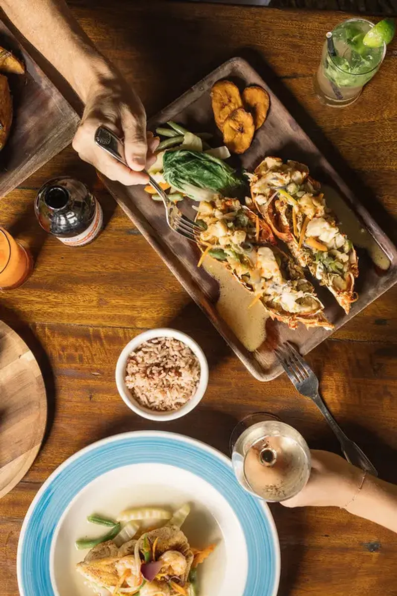 Overhead table lay of the grilled lobster with a side of rice and peas and a cold glass of crisp white wine at the Rockhouse Restaurant at Rockhouse Hotel in Negril, Jamaica.