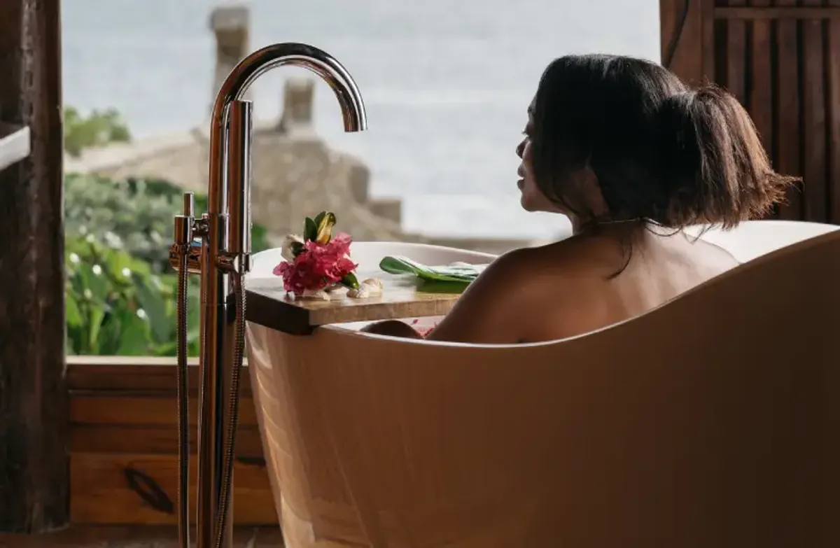 Young woman enjoying a cliffside bath at Rockhouse Hotel in Negril, Jamaica, with a stunning view of the turquoise Caribbean Sea—a moment of relaxation and luxury.
