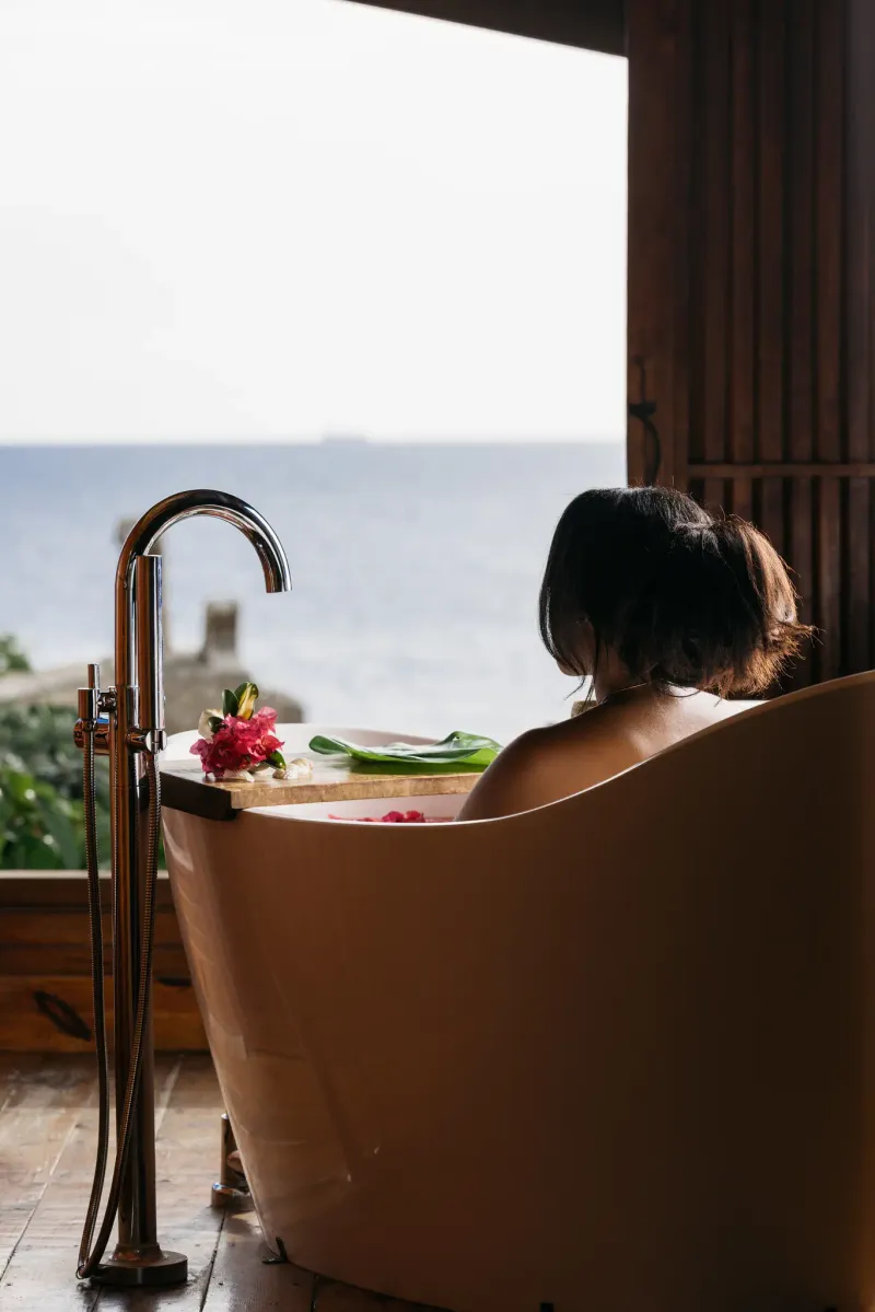 A close-up shot of an outdoor shower with a stream of water, featuring intricate blue tile work and a rustic thatched roof at Rockhouse Hotel in Negril, Jamaica, highlighting the hotel's unique and natural bathroom designs.