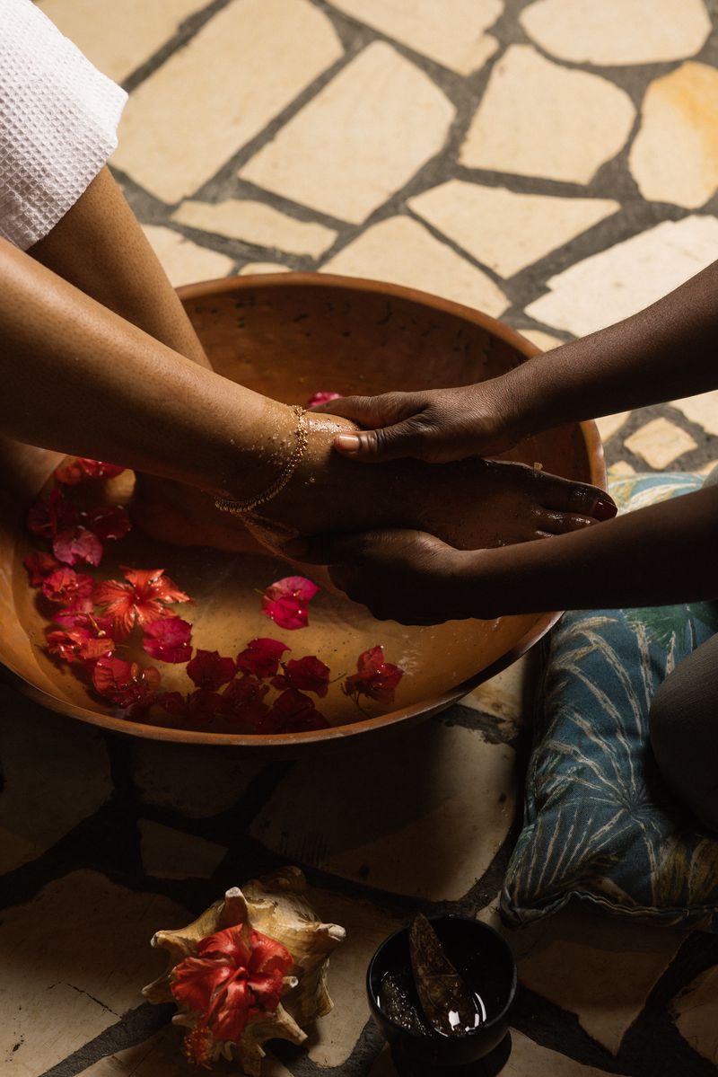 A soothing foot-washing ritual with hands gently massaging a guest’s foot over a bowl filled with warm water and vibrant pink petals at Rockhouse Hotel in Negril, Jamaica.