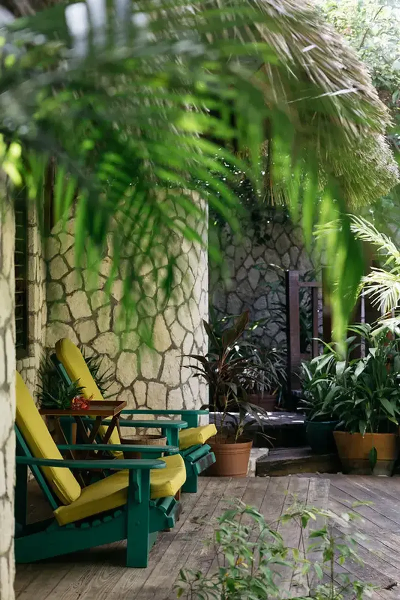 Green lounge chairs on a wooden deck surrounded by lush tropical plants and stone walls, at Rockhouse Hotel in Negril, Jamaica, highlighting a private and relaxing villa patio at Rockhouse Hotel.