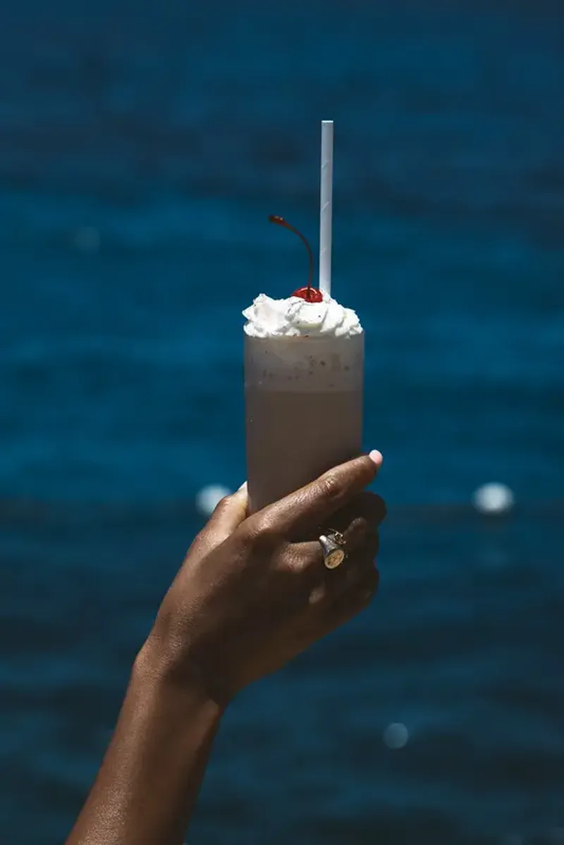Chocolate milkshake with whipped cream and a cherry on top, served by the ocean at Rockhouse Hotel in Negril, Jamaica, highlighting a refreshing poolside drink at Rockhouse Hotel.