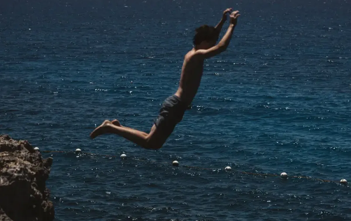 Person in mid-air jumping from the cliffs at Rockhouse Hotel in Negril, Jamaica, captured just before hitting the deep blue water—a classic Jamaican cliff-jumping experience.