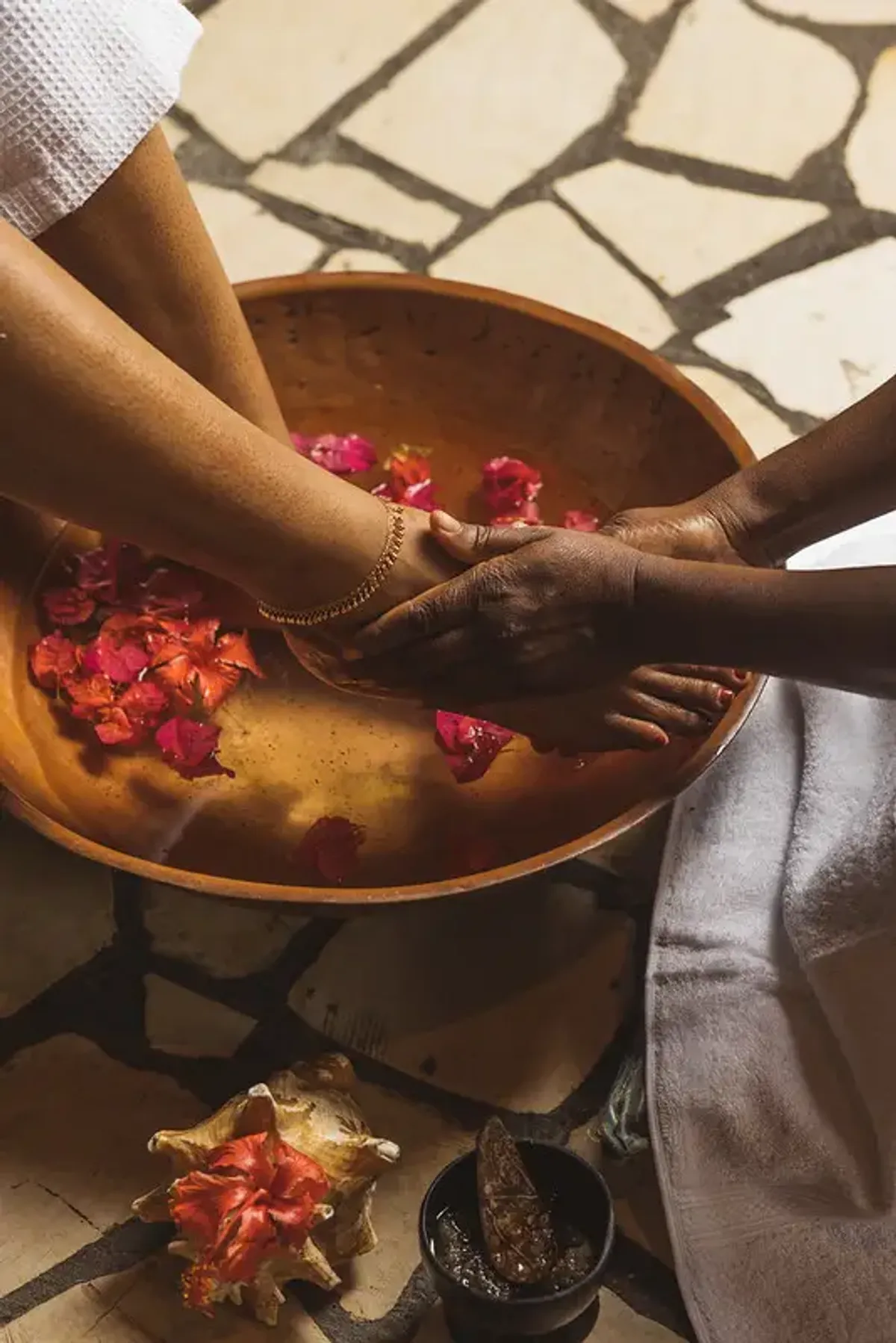 Spa technician giving a foot bath with flowers to a client in a wooden bowl at Rockhouse Hotel in Negril, Jamaica, highlighting a restorative spa experience at Rockhouse Hotel.