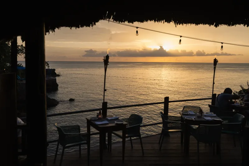 A view from a cliffside dining table elegantly set on the water on Vincent's Deck at Rockhouse Restaurant nightstand showcasing the unique, natural beauty of dining at Rockhouse Hotel in Negril, Jamaica.