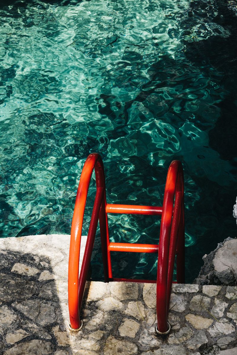 Bright red ladder leading into the clear turquoise water at Rockhouse Hotel in Negril, Jamaica, set against natural stone and sunlit ripples.