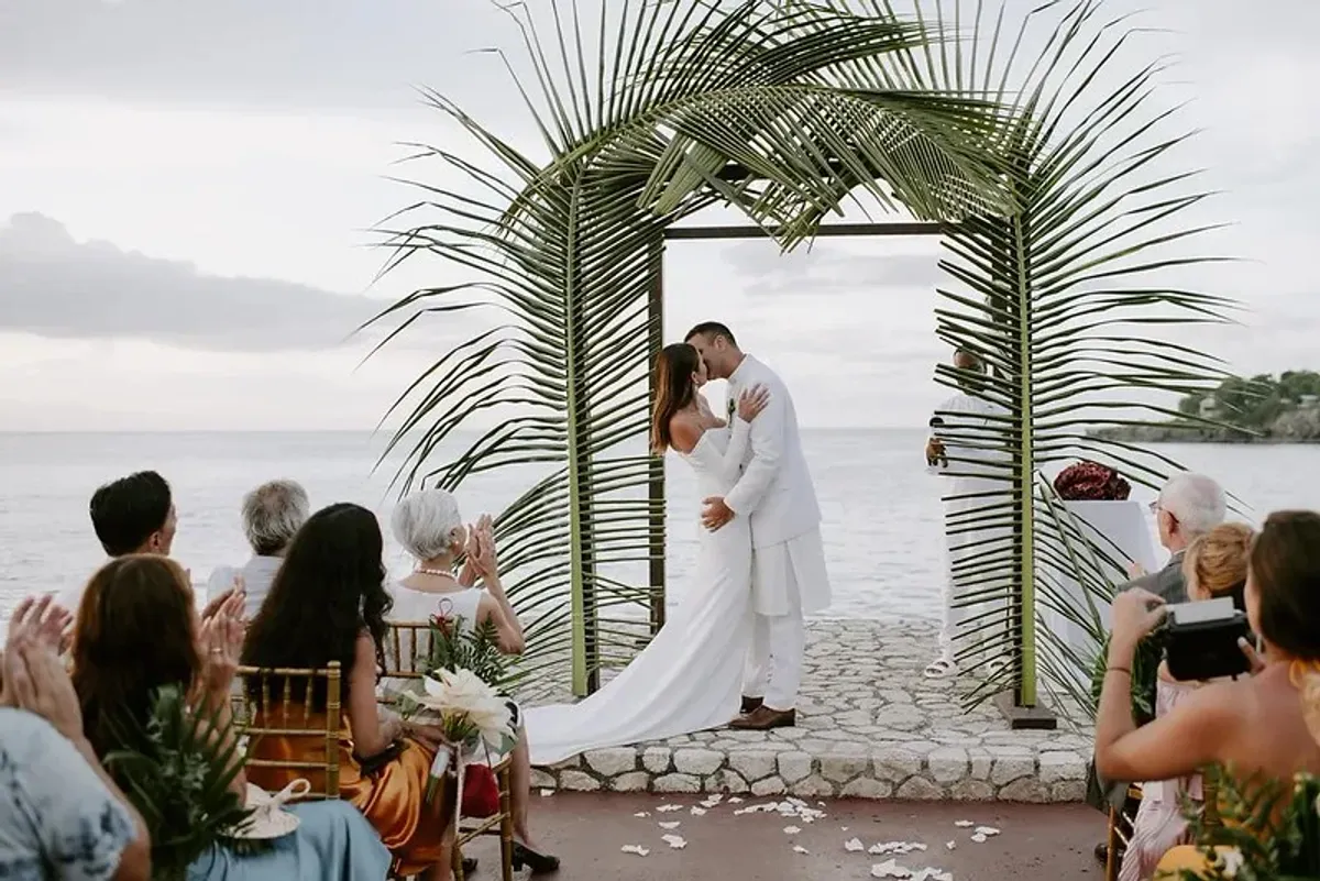 Image of a bride and groom standing under a bridal arch overlooking the ocean at a wedding ceremony at Rockhouse Hotel in Negril, Jamaica, highlighting a romantic wedding venue at Rockhouse Hotel.