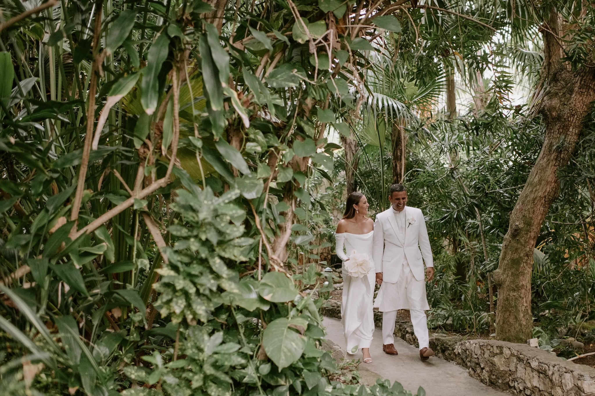 Newlyweds walking hand in hand through the lush tropical gardens at Rockhouse Hotel in Negril, Jamaica, surrounded by dense greenery as they share a joyful, intimate moment on their wedding day.