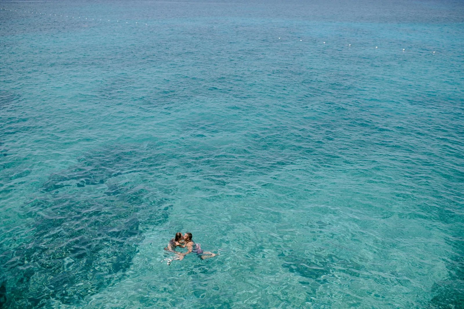 Couple floating together in the crystal-clear turquoise water at Rockhouse Hotel in Negril, Jamaica, surrounded by the calm, shimmering Caribbean Sea.