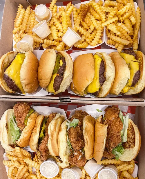 A delicious assortment of cheeseburgers, crispy chicken sandwiches, and crinkle-cut fries from The Meat Up Grill, showcasing a classic American comfort food feast.