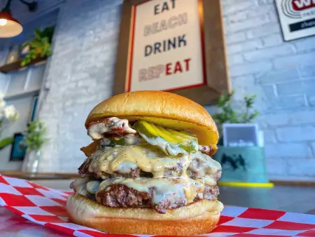 Towering cheeseburger loaded with multiple patties, melted cheese, and pickles from The Meat Up Grill, a true indulgence.
