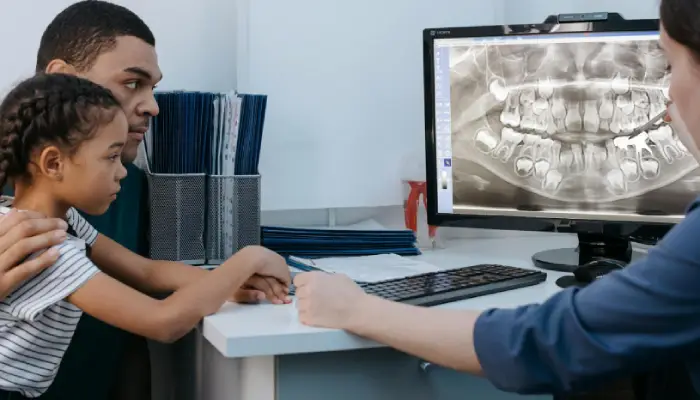 Dentist showing a young girl and her father a digital dental X-ray at East End Tooth Ferry pediatric dental office in Southampton, New York