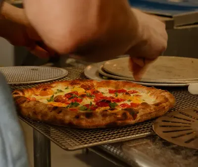 Chef finishing a freshly baked Neapolitan pizza topped with tomatoes, basil, and mozzarella at Anna’s Vesuviano in Providence, Rhode Island