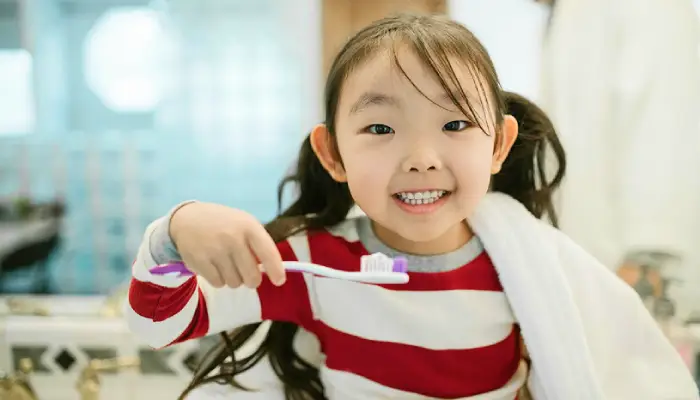 Smiling young girl brushing her teeth, promoting good dental hygiene at East End Tooth Ferry pediatric dentist in Southampton, New York.