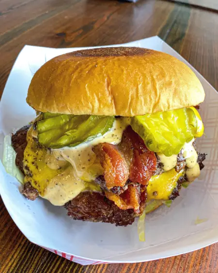 Classic cheeseburger with crispy bacon, melted cheese, and pickles served in a soft bun from The Meat Up Grill.