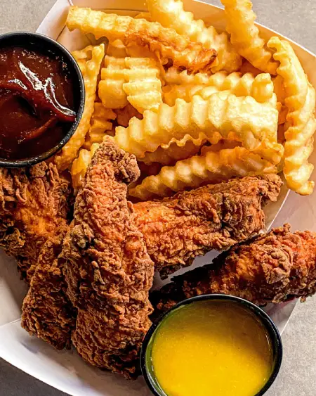 Golden crinkle-cut fries with crispy fried chicken tenders served with dipping sauce from The Meat Up Grill.