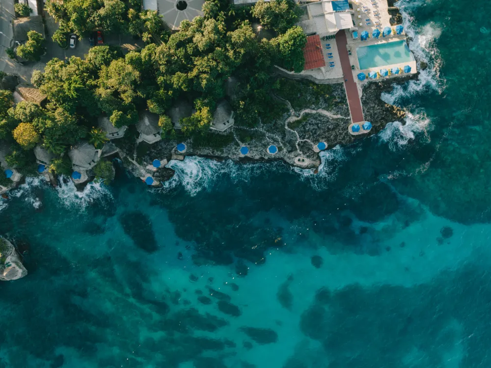 Aerial view of Rockhouse Hotel perched on the cliffs of Negril, Jamaica, featuring private villas, lush tropical gardens, and an oceanfront infinity pool overlooking the turquoise Caribbean Sea