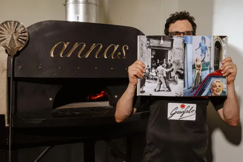 Chef at Anna’s Vesuviano holding an open book of Italian culture photos in front of the wood-fired oven, symbolizing the restaurant’s roots in Italian tradition and artistry