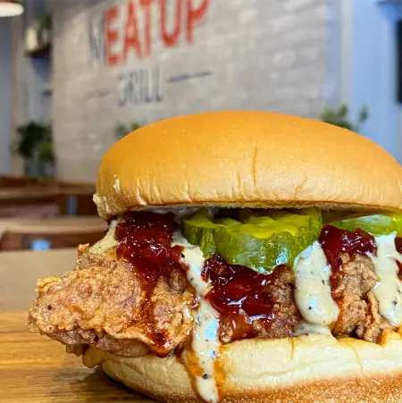 Crispy fried chicken sandwich topped with pickles and barbecue sauce from The Meat Up Grill, packed in a fluffy bun.
