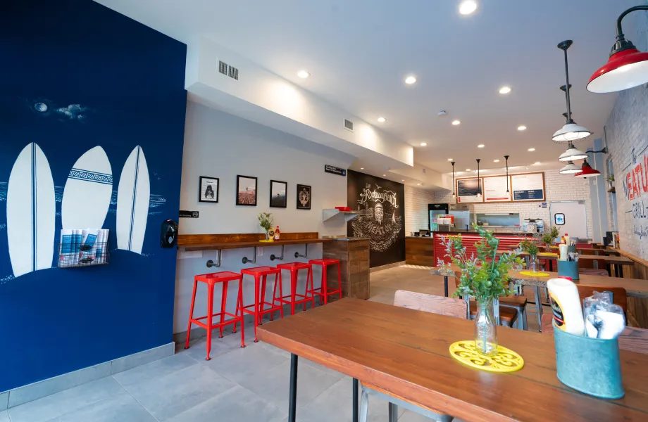 Interior of The Meat Up Grill in Rockaway Beach, featuring surfboard-themed decor, vibrant red stools, and a welcoming dining area with a modern, beach-inspired design