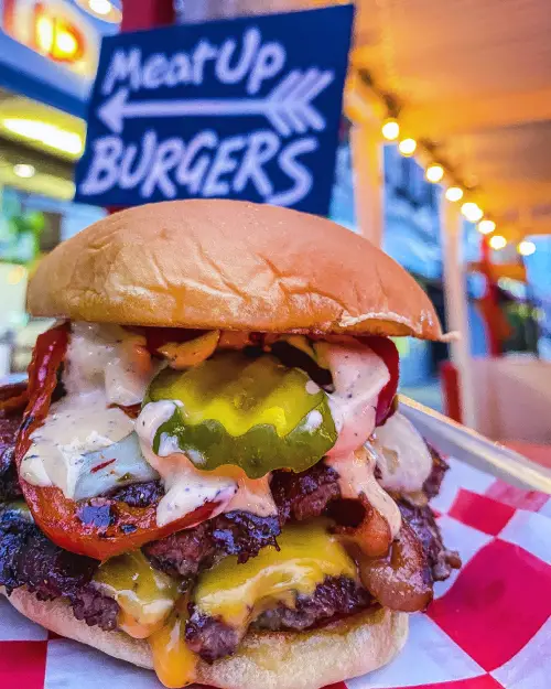 Juicy cheeseburger stacked with melted cheese, crispy bacon, and pickles from The Meat Up Grill, served with a rich savory flavor.