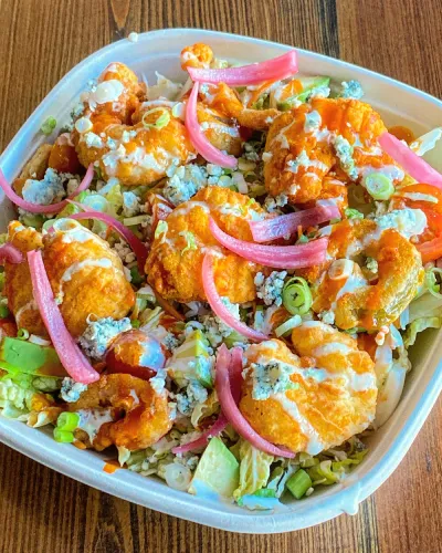 A vibrant salad from The Meat Up Grill, featuring crispy buffalo chicken, pickled onions, blue cheese crumbles, and fresh greens, showcasing a flavorful and colorful dish.