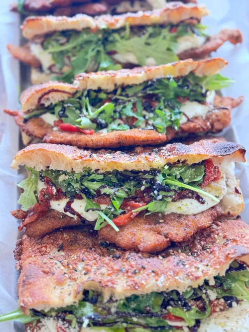 Stacked Italian sandwiches on focaccia bread from Crustinos Pizza, loaded with fresh ingredients.