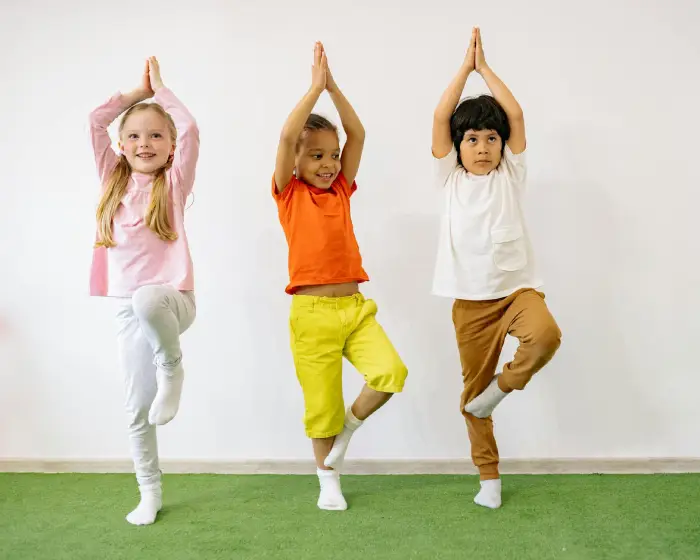 Three smiling children practicing yoga poses together at East End Tooth Ferry pediatric dental office in Southampton, New York.