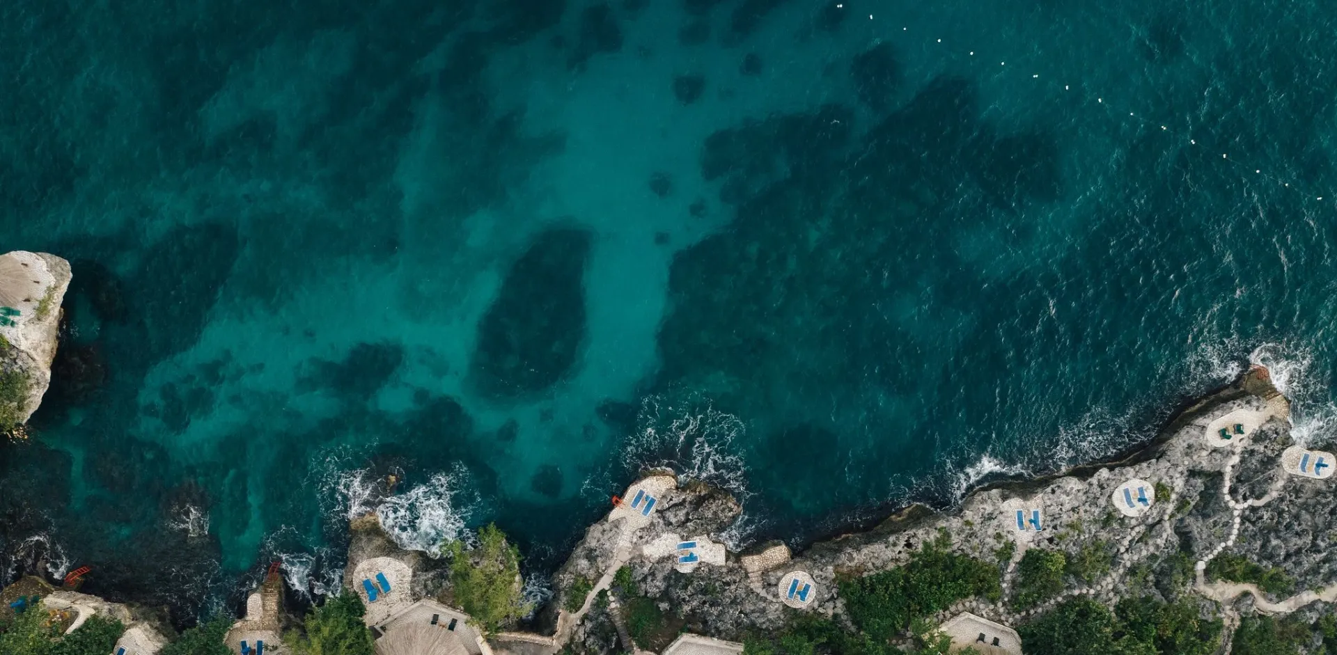 Aerial view of Rockhouse Hotel’s cliffside sun decks and turquoise Caribbean Sea in Negril, Jamaica, highlighting luxury resort amenities and natural beauty