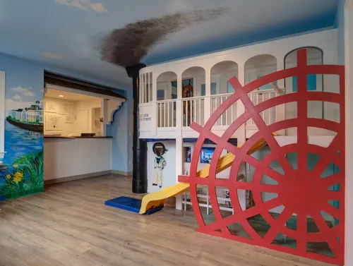 Playful steamboat-themed interior at East End Tooth Ferry pediatric dental office in Southampton, New York, featuring a red paddle wheel structure, slide, and nautical wall mural near the reception area