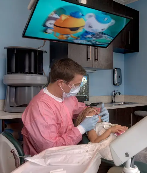 Dr. Greg Reinhold, pediatric dentist at East End Tooth Ferry in Southampton, New York, examining a young patient while a cartoon plays on the ceiling screen.