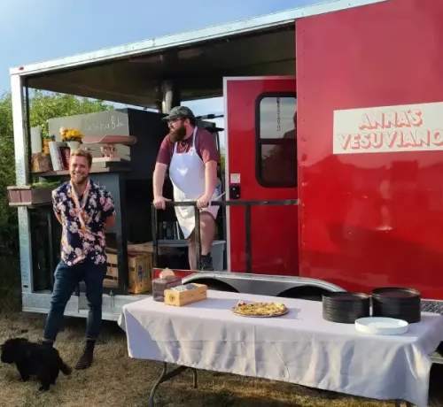 Team members of Anna’s Vesuviano standing beside the red mobile pizza trailer, serving freshly baked wood-fired pizza at an outdoor event in Providence, Rhode Island