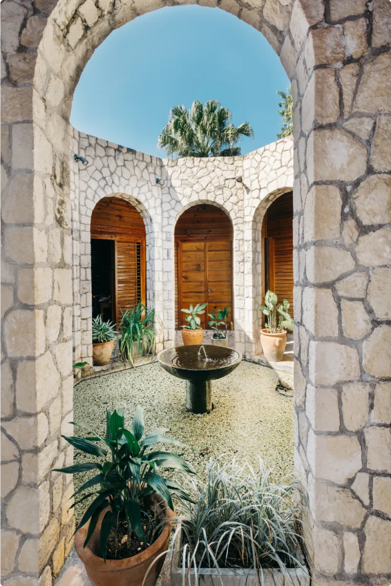 Tranquil stone courtyard with tropical plants and a central fountain at Rockhouse Hotel spa in Negril, Jamaica, offering guests a serene oasis for relaxation and wellness retreats.