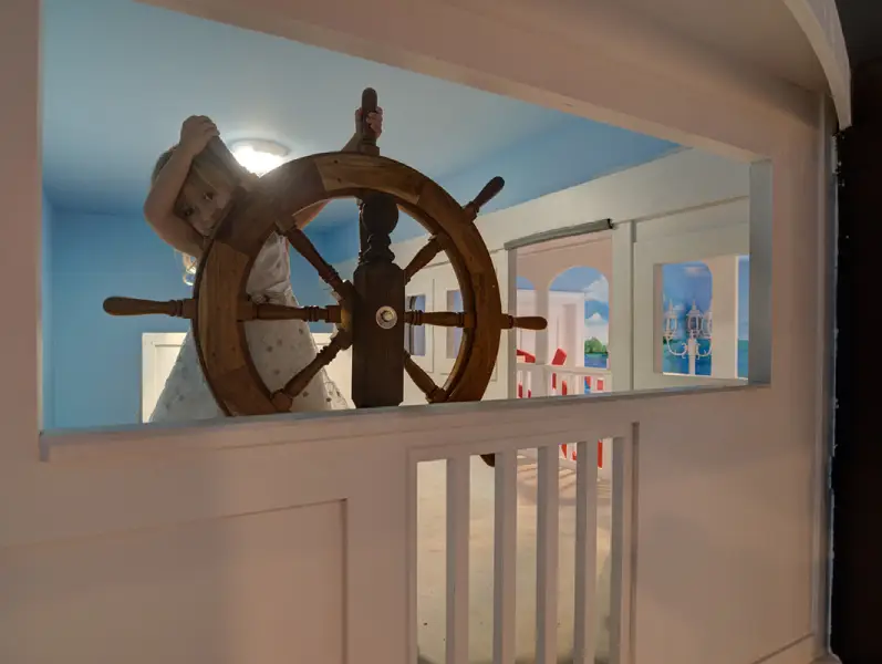 A young child happily playing with a large wooden ship wheel in a nautical-themed pediatric dental office at East End Tooth Ferry in Southampton, NY.