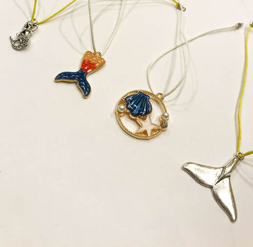 Assorted ocean-themed Good Luck Wish Band charms from Dr. Greg at East End Tooth Ferry, featuring mermaid tails and seashell designs.