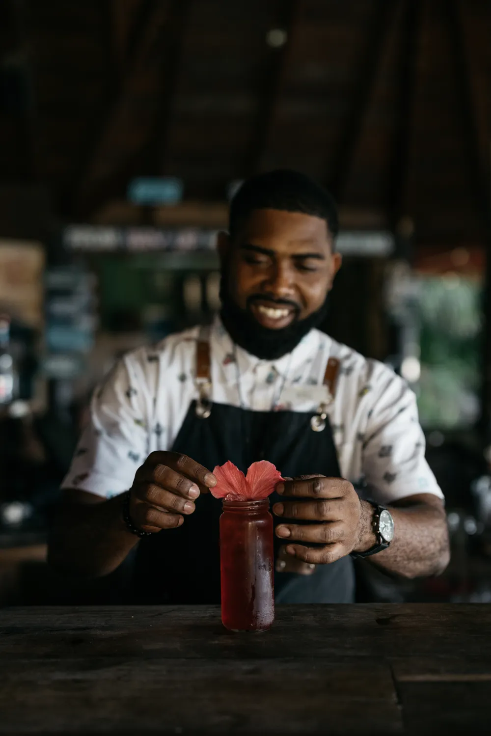 Bartender at Rockhouse Hotel in Negril, Jamaica, garnishing a vibrant red cocktail with a fresh hibiscus flower, showcasing the resort's tropical and creative drink offerings.